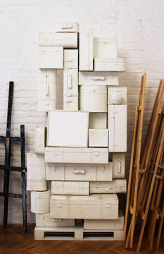 A lot of white suitcases of different shapes are stacked on each other and a picture in the form of a light gray rectangle against a white brick wall