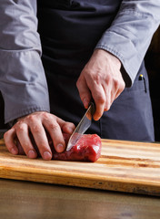 Chef cutting filet mignon on wooden board at restaurant kitchen