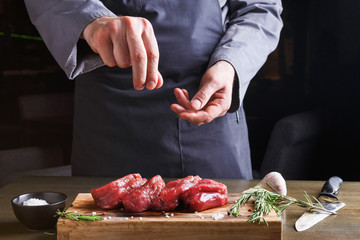 Chef seasoning filet mignon on wooden board at restaurant kitchen