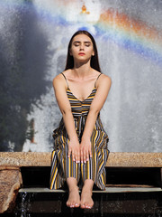 Girl brunette model sitting with closed eyes and posing near with rainbow