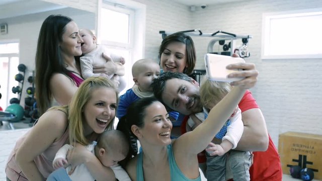 Young parents and babies in modern gym taking selfie.