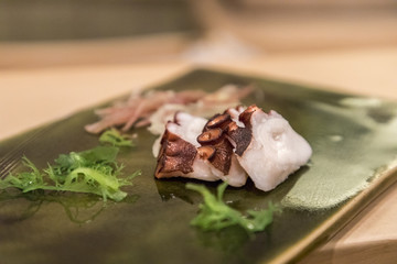 Fresh three slices of sashimi octopus on green plate with green leaves closeup