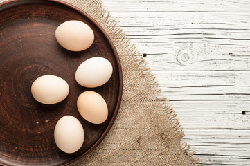 chicken eggs in clay plate on white wooden background