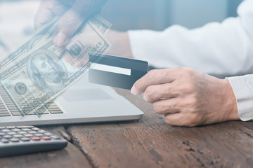 Hands holding credit card and using laptop,double exposure with hands holding cash us dollar..Man shopping online at restaurant,online business concept..