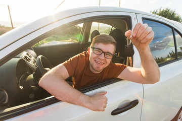 Naklejka premium Happy young smiling man sitting inside new car with keys.