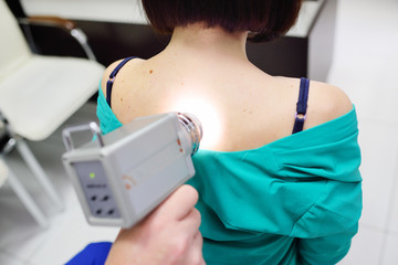 The doctor examines neoplasms or moles on the patient's skin - a young girl using a special apparatus for dermatoscopy - a dermoscope. Prevention of melanoma and skin cancer.