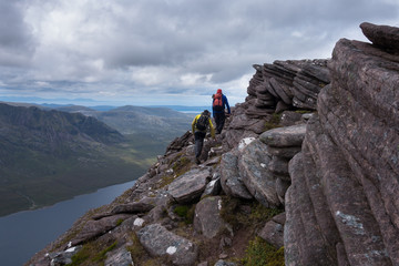 Two walkers travering ridge trail overlooking lake in Scottish Highlands