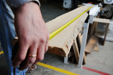The joiner makes the marking of the board with a measuring tape measure on the background of the joiner's workshop