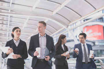 Happy Business colleagues walking outside office & talking to each other. Businessman talk and hold coffee cup