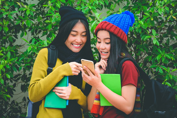 Fototapeta premium Two young asian travelers who are wearing colorful clothes with beanies and scarves are searching the information or checking the location on the phone