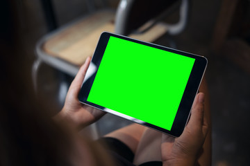 Mockup image of woman's hands holding black tablet pc with blank grren screen on thigh with concrete floor background in modern cafe