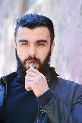 Bearded young man smokes an electronic cigarette or vape