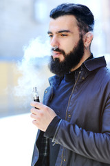 Young stylish bearded man in a black hat with an electronic cigarette or vape