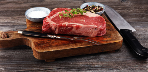 Raw fresh meat Ribeye Steak, seasoning and meat fork on dark background