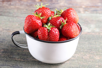 Fresh strawberries in cup on grey wooden table