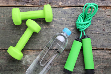 Green skipping rope with bottle of water and dumbbells on wooden table