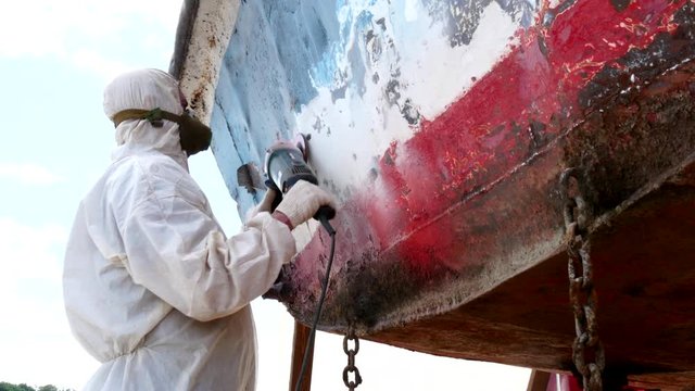 Working people tear off paint on metal in repairs process at shipyard. Workers in overalls reconstruct at ship repair yard outdoors in port.