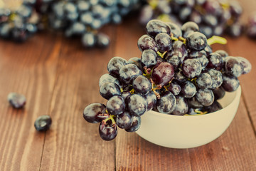 Black grape branch in bowl on dark wooden background