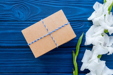 Preparing to celebration. Box in kraft paper near flower gladiolus on blue wooden table top view copyspace