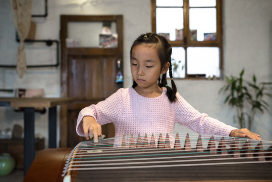Adorable little girl playing zither at home