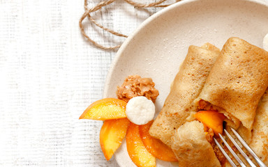 Homemade pancakes or russian blini With peach, honey and peanut butter on plate on rustic wooden...