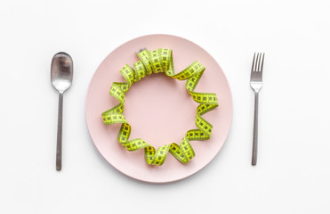 Slimming diet. Measuring tape at empty plate on white background top view