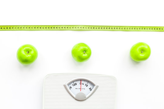 Bathroom scale, measuring tape and apples on white background top view