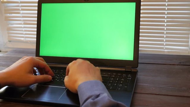 businessman typing on a laptop keyboard with chrome key. blank display with green screen for your presentation. closeup shot with dim light
