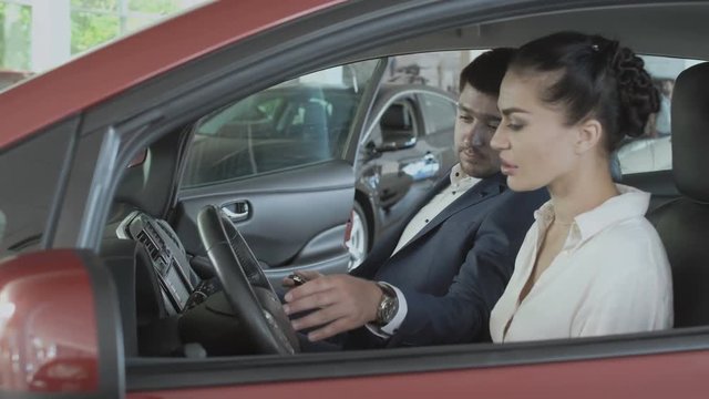 Beautiful woman inspects the car's cabin in car showroom with salesman