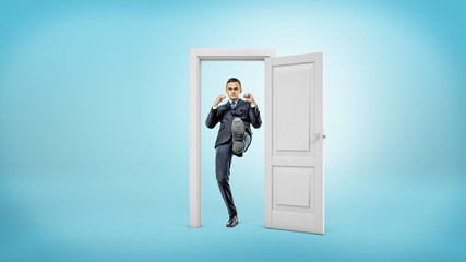A young businessman stands in a small cut out doorframe and kicks a door open with his foot.