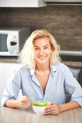 Young blonde girl sitting at the Breakfast table in the kitchen