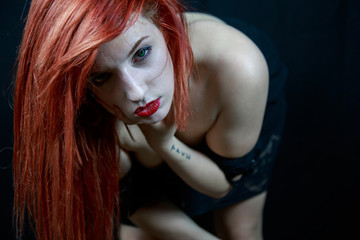 Portrait of woman with makeup posing while undressing and bending forward on black background. 