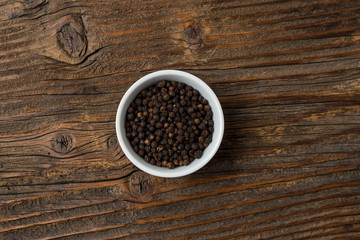 Black pepper in white bowl on an old wooden table