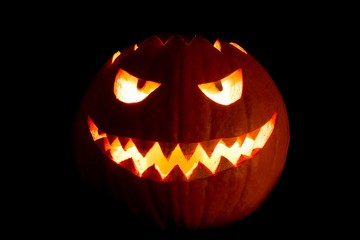 Round halloween pumpkin smile with hot burning fire eyes mouth. The big helloween symbol has a mad face glowing eyes and also a glow in its mouth and teeth. Black orange nightmare of October 31st