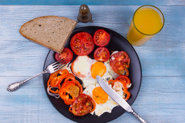 Scrambled eggs with tomatoes and orange juice on a rustic wooden background