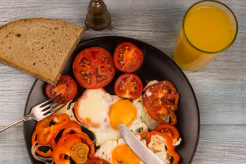 Scrambled eggs with tomatoes and orange juice on a rustic wooden background