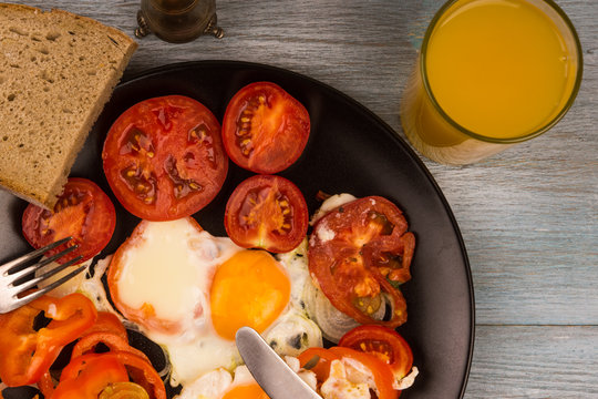 Scrambled eggs with tomatoes and orange juice on a rustic wooden background
