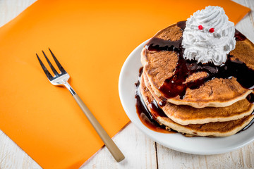 Ideas for children's breakfast, treats for Thanksgiving and Halloween. Pancakes with chocolate sauce and whipped cream in the form of a ghost. On a white wooden table, copy space