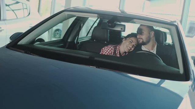 Happy couple kisses and enjoys a new automobile in the car dealership