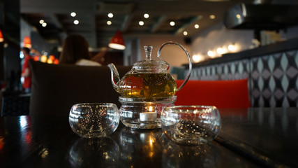 Two glass cups of herbal tee stay on a dark black wood table. Behind of caps a beautifull candle under a glass cover. Everything is in deep dark colors under a warm light. Romantic time.