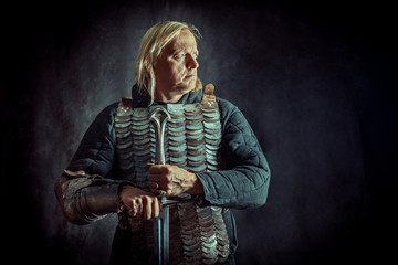 Powerful blond knight with the sword on the dark background.