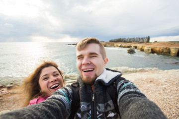 Fototapeta na wymiar Happy young couple in love takes selfie portrait on the beach in Cyprus in autumn or winter. Pretty tourists make funny photos for travel blog in Europe.
