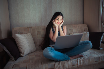 Young beautiful brunette watching movie on laptop at home at night