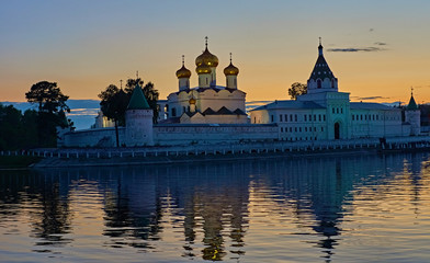 Obraz premium Monastery in the rays of sunset/Ipatievsky Monastery in Kostroma. The domes are illuminated with searchlights.The monastery is on the river bank and is reflected in the river.Golden Ring of Russia