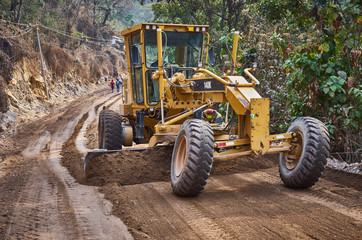 Heavy machine on road construction in Guatemala / Grader pushing dirt to level the dirt road 