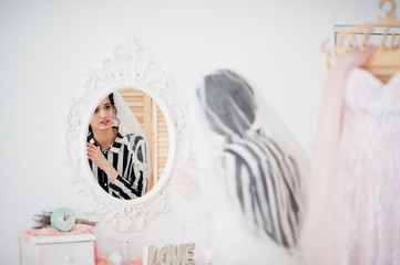 Portrait of a gorgeous bride looking in the mirror and putting on her wedding earrings.