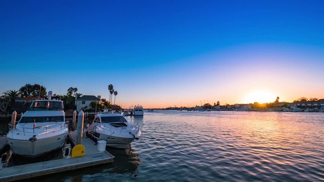 Cinematic timelapse shot at sunset over the harbor water in Newport Beach, California with boats, yachts and luxury real estate in view.