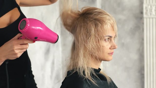 Hairdresser blows hair into the hair of a young blond girl in the salon