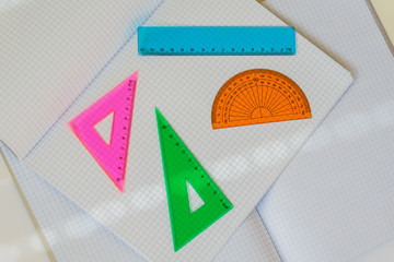 Close-up of set of colored instruments for geometry on background of large open empty notebooks in...