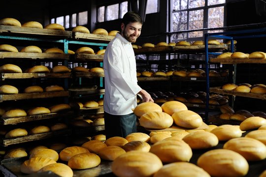 young cute baker smiling pulls out of the oven fresh bread shovel bread